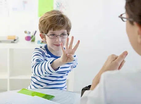 A young boy with glasses and a striped shirt holding up 4 fingers while engaged n speech therapy at Whiz Kids Tutoring