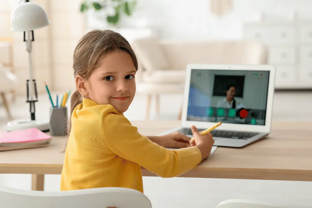 Child engaged in virtual learning session with notebook and laptop in a clean workspace