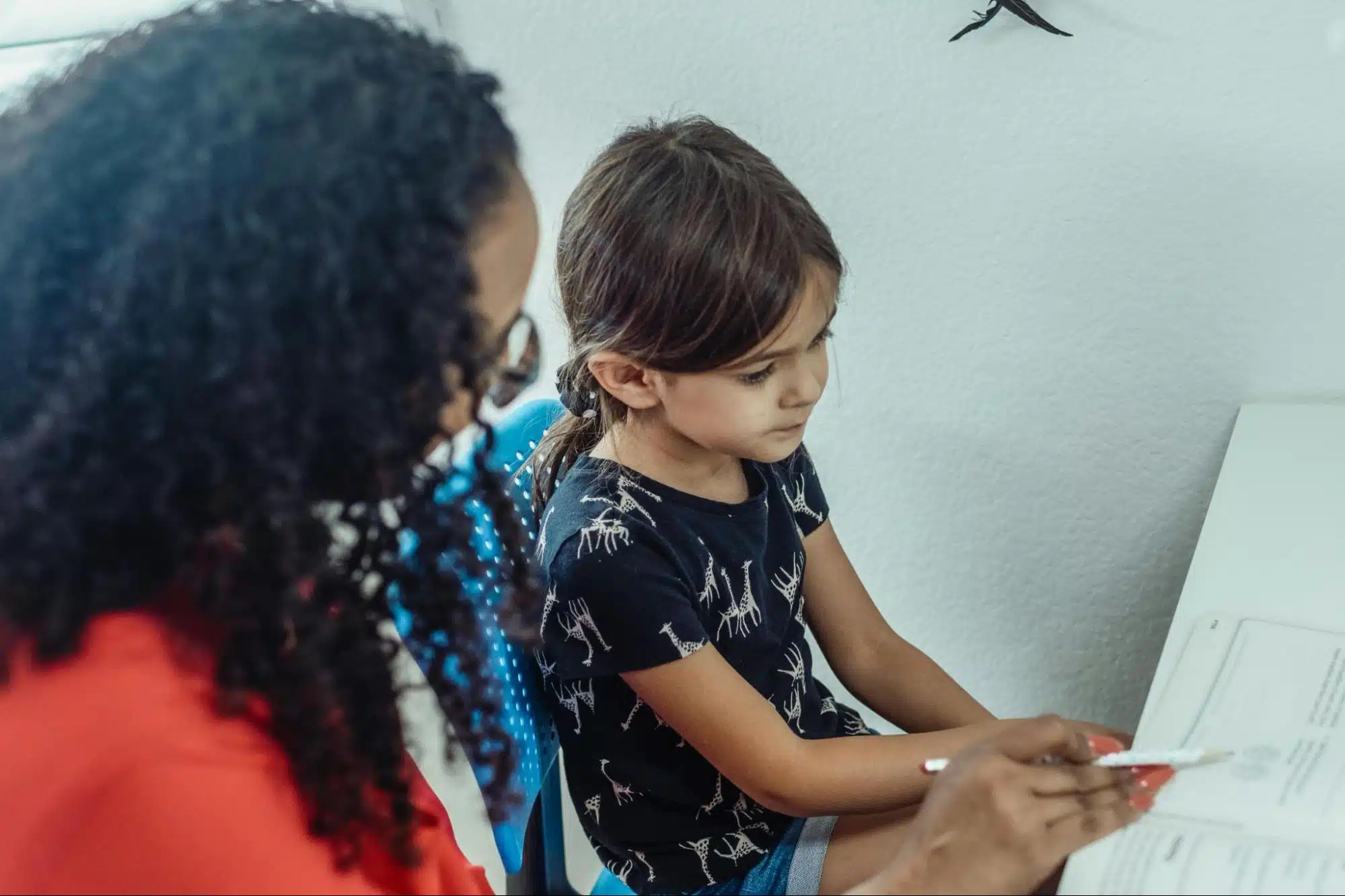A teacher guiding a young girl through a workbook lesson