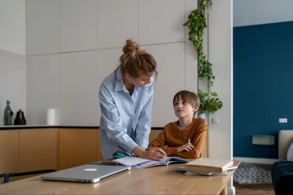 Female tutor pointing at a workbook while explaining a lesson to a boy